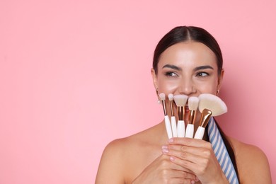 Photo of Beautiful woman with makeup brushes on pink background, space for text