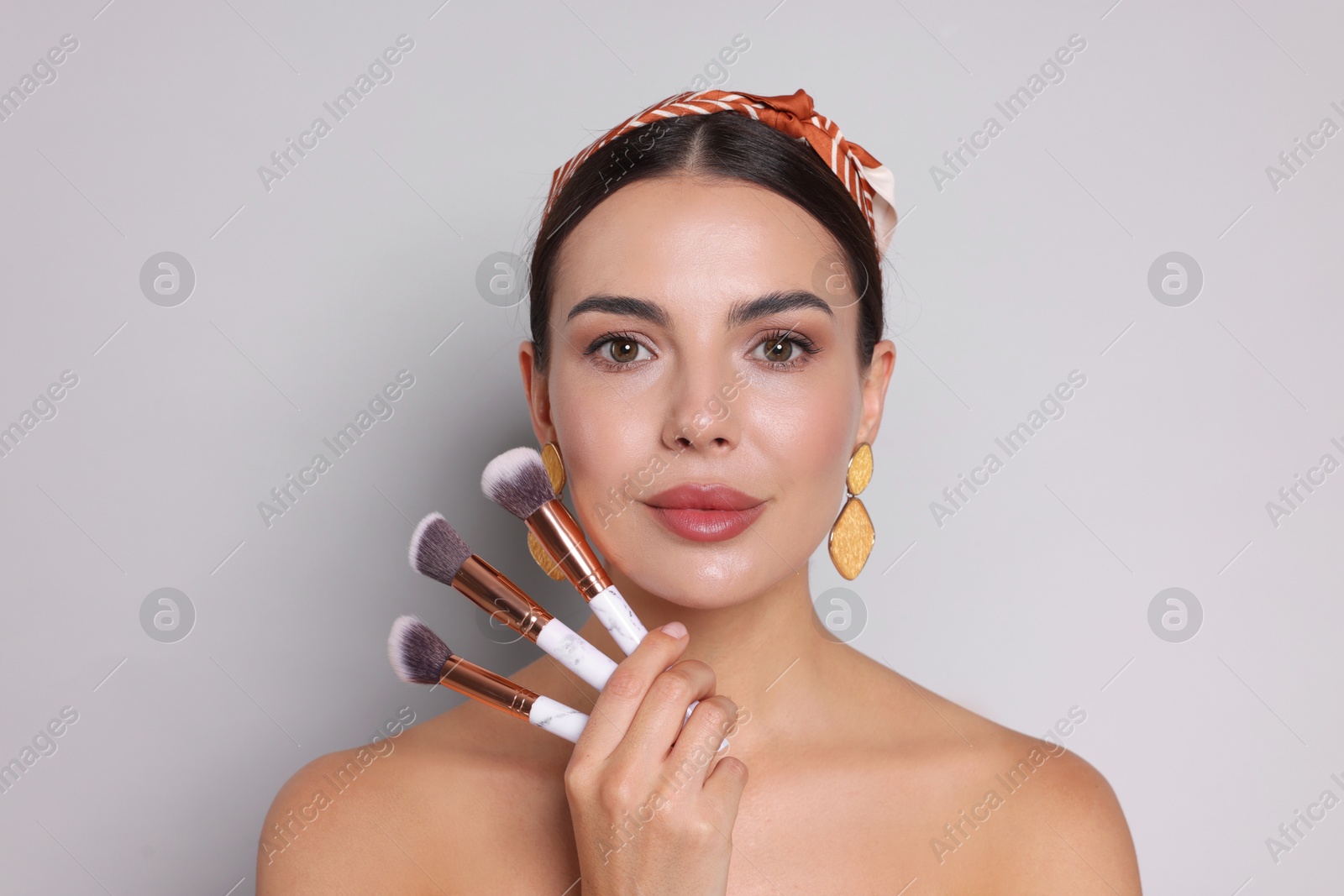 Beautiful woman with makeup brushes on light grey background Photo of Beautiful woman with makeup brushes on light grey background