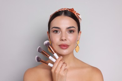 Photo of Beautiful woman with makeup brushes on light grey background