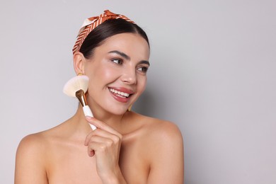 Photo of Beautiful woman with makeup brush on light grey background, space for text
