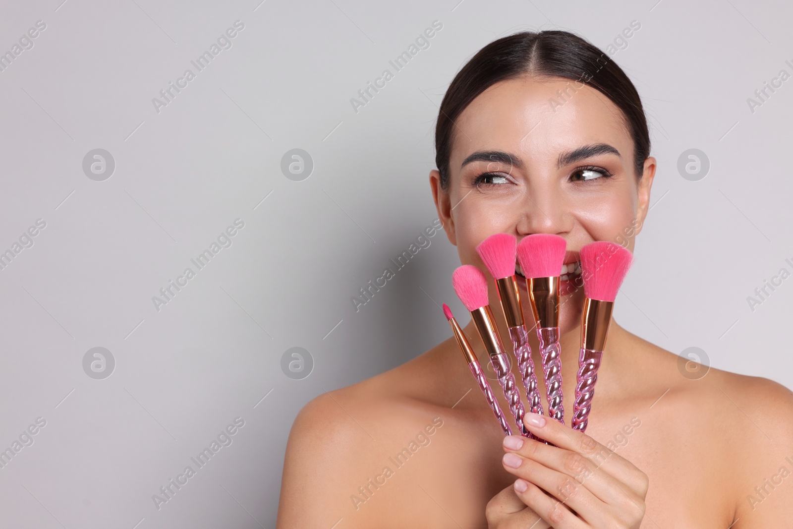 Beautiful woman with makeup brushes on light grey background, space for text Photo of Beautiful woman with makeup brushes on light grey background, space for text