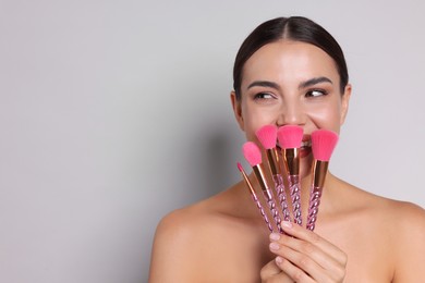 Photo of Beautiful woman with makeup brushes on light grey background, space for text