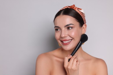 Photo of Beautiful woman with makeup brush on light grey background, space for text