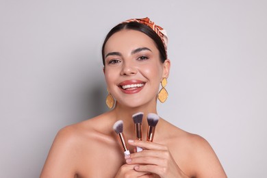 Photo of Beautiful woman with makeup brushes on light grey background