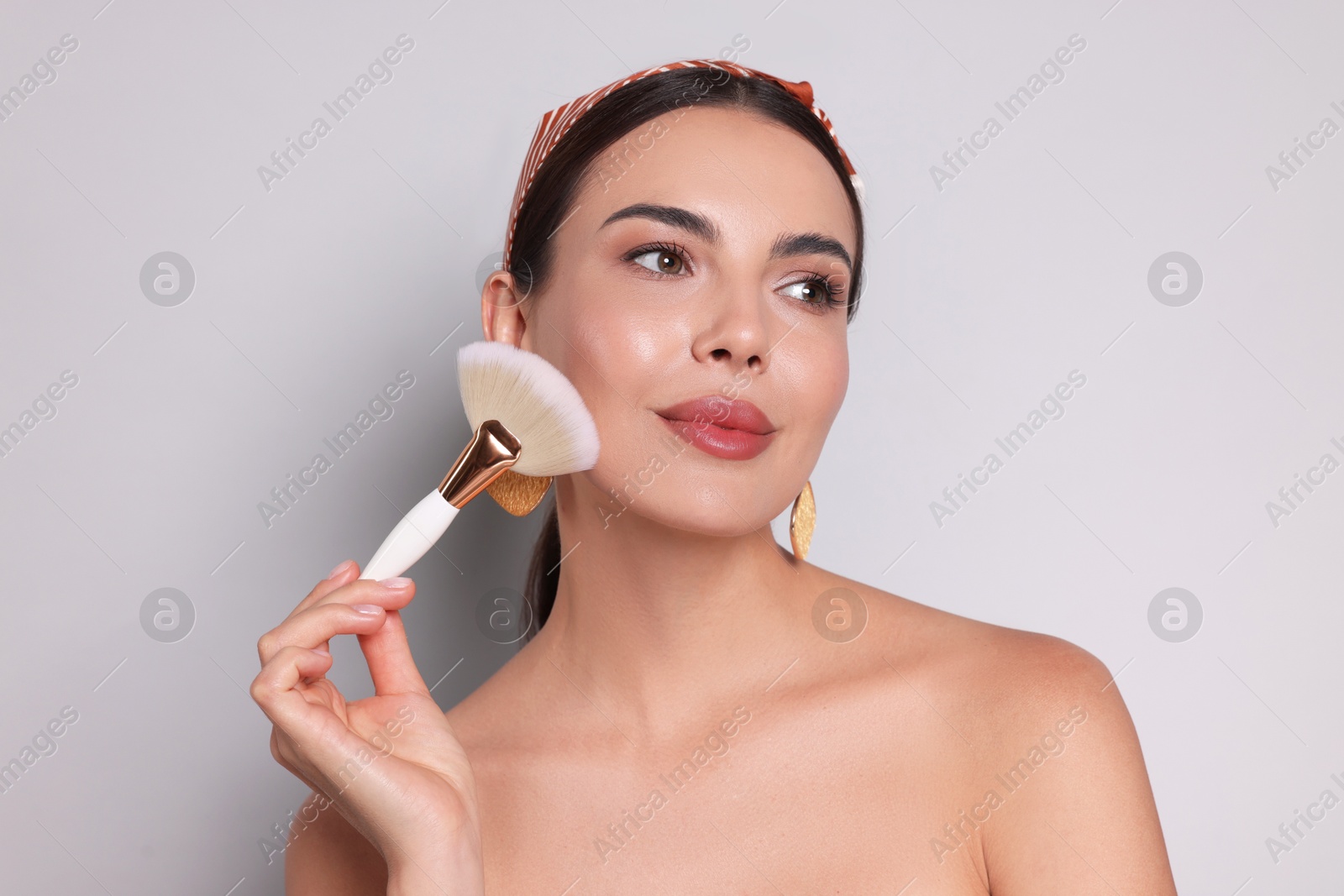 Photo of Beautiful woman applying makeup with brush on light grey background