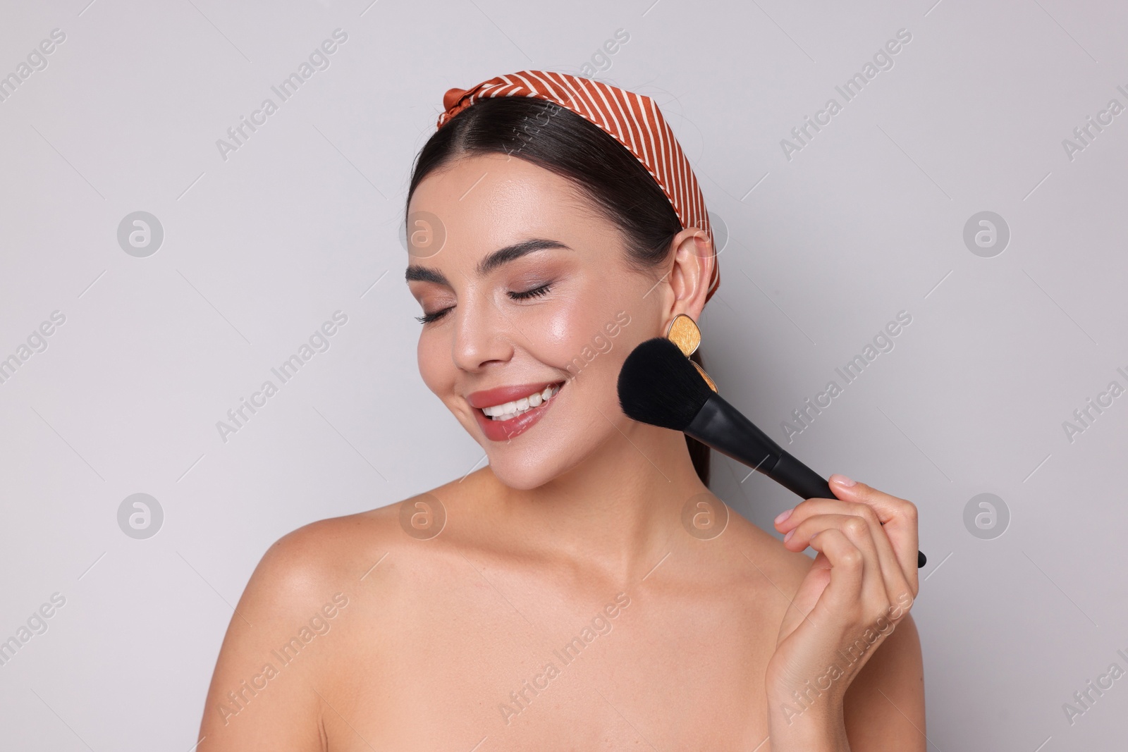 Photo of Beautiful woman applying makeup with brush on light grey background