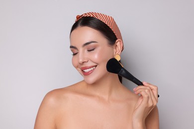 Photo of Beautiful woman applying makeup with brush on light grey background