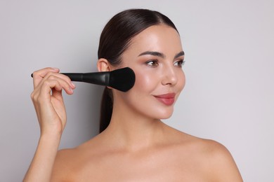 Photo of Beautiful woman applying makeup with brush on light grey background