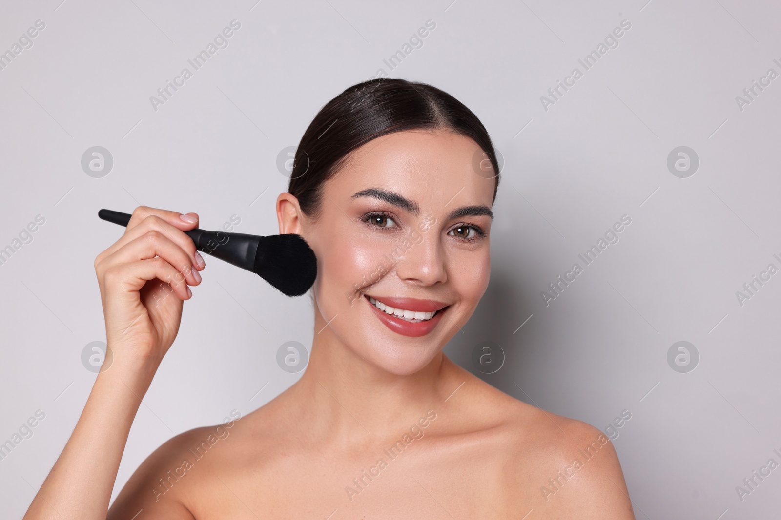 Photo of Beautiful woman applying makeup with brush on light grey background