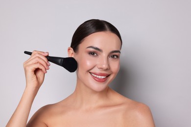 Photo of Beautiful woman applying makeup with brush on light grey background