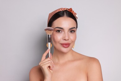 Photo of Beautiful woman with makeup brush on light grey background