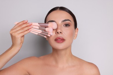 Photo of Beautiful woman with makeup brushes on light grey background