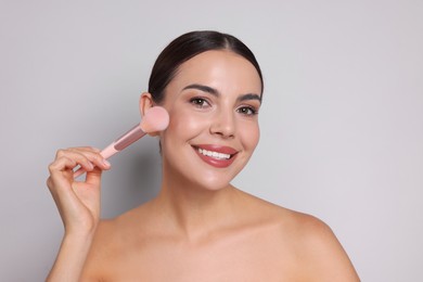 Photo of Beautiful woman applying makeup with brush on light grey background