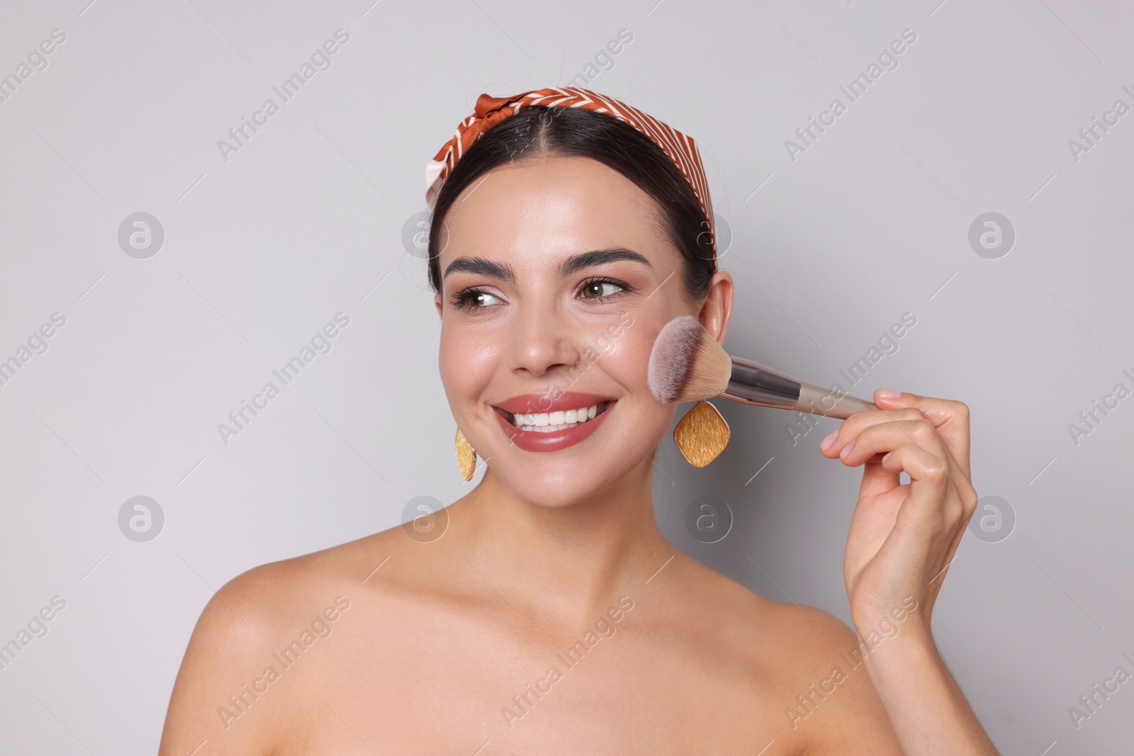Beautiful woman applying makeup with brush on light grey background Photo of Beautiful woman applying makeup with brush on light grey background