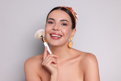 Photo of Beautiful woman with makeup brush on light grey background