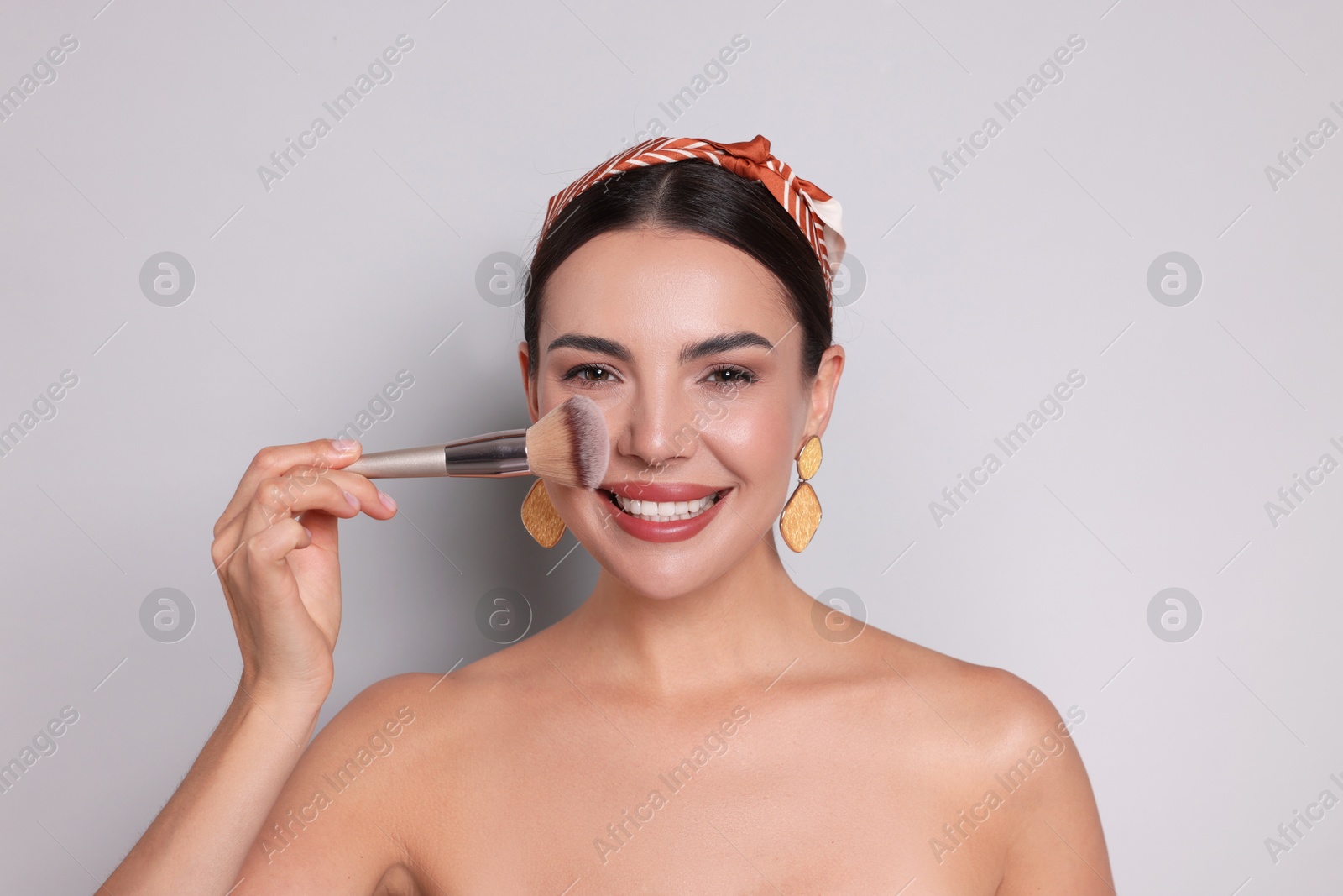 Beautiful woman applying makeup with brush on light grey background Photo of Beautiful woman applying makeup with brush on light grey background