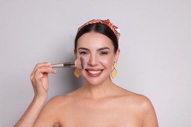 Photo of Beautiful woman applying makeup with brush on light grey background