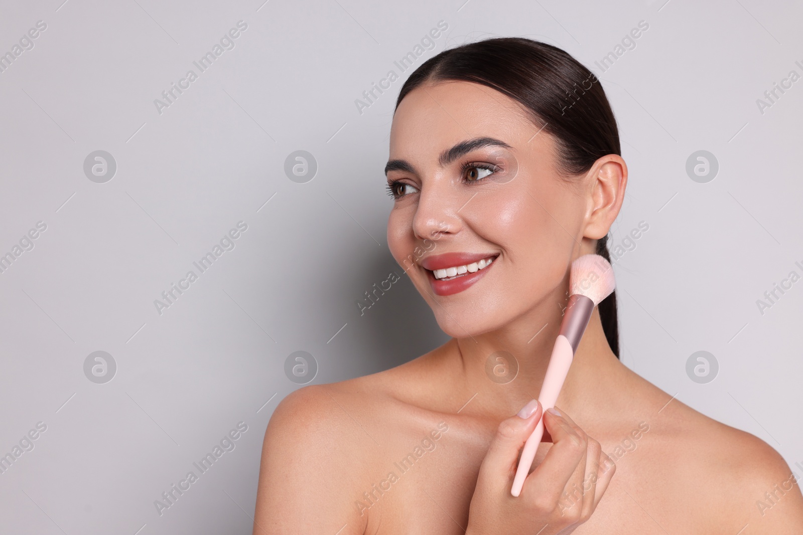 Photo of Beautiful woman with makeup brush on light grey background, space for text