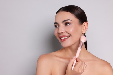 Photo of Beautiful woman with makeup brush on light grey background, space for text