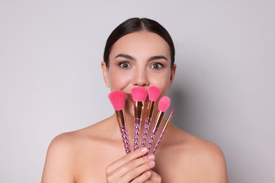 Photo of Beautiful woman with makeup brushes on light grey background