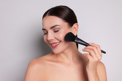 Photo of Beautiful woman applying makeup with brush on light grey background