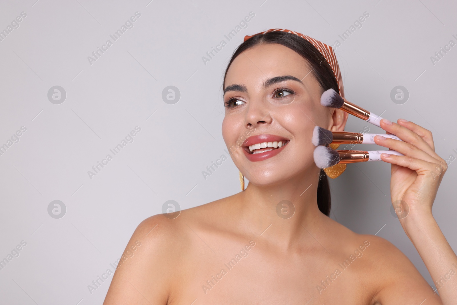 Beautiful woman with makeup brushes on light grey background, space for text Photo of Beautiful woman with makeup brushes on light grey background, space for text
