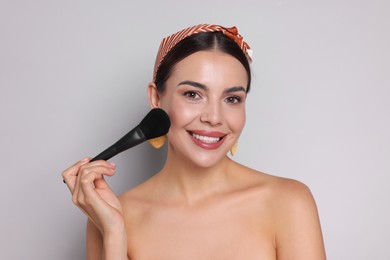 Photo of Beautiful woman applying makeup with brush on light grey background