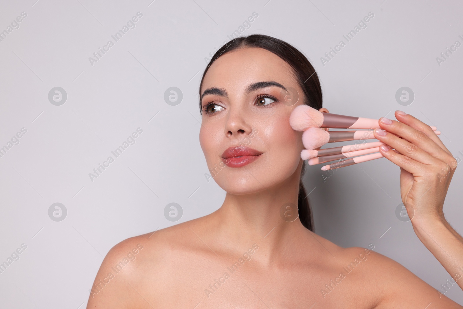 Beautiful woman with makeup brushes on light grey background, space for text Photo of Beautiful woman with makeup brushes on light grey background, space for text