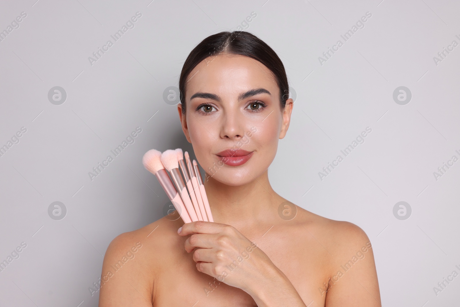 Photo of Beautiful woman with makeup brushes on light grey background