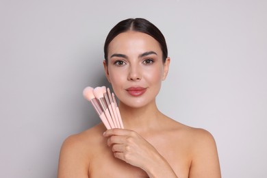 Photo of Beautiful woman with makeup brushes on light grey background
