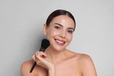 Photo of Beautiful woman with makeup brush on light grey background