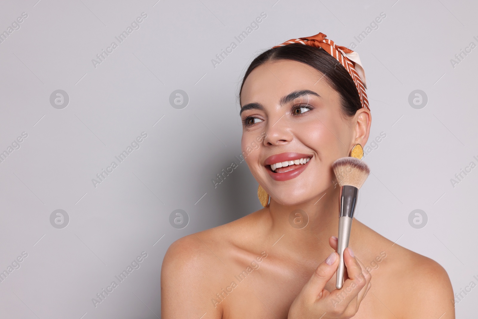 Photo of Beautiful woman with makeup brush on light grey background, space for text