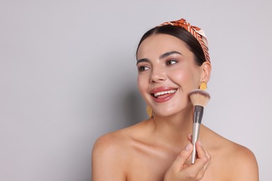 Photo of Beautiful woman with makeup brush on light grey background, space for text