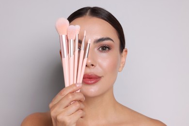 Photo of Beautiful woman with makeup brushes on light grey background