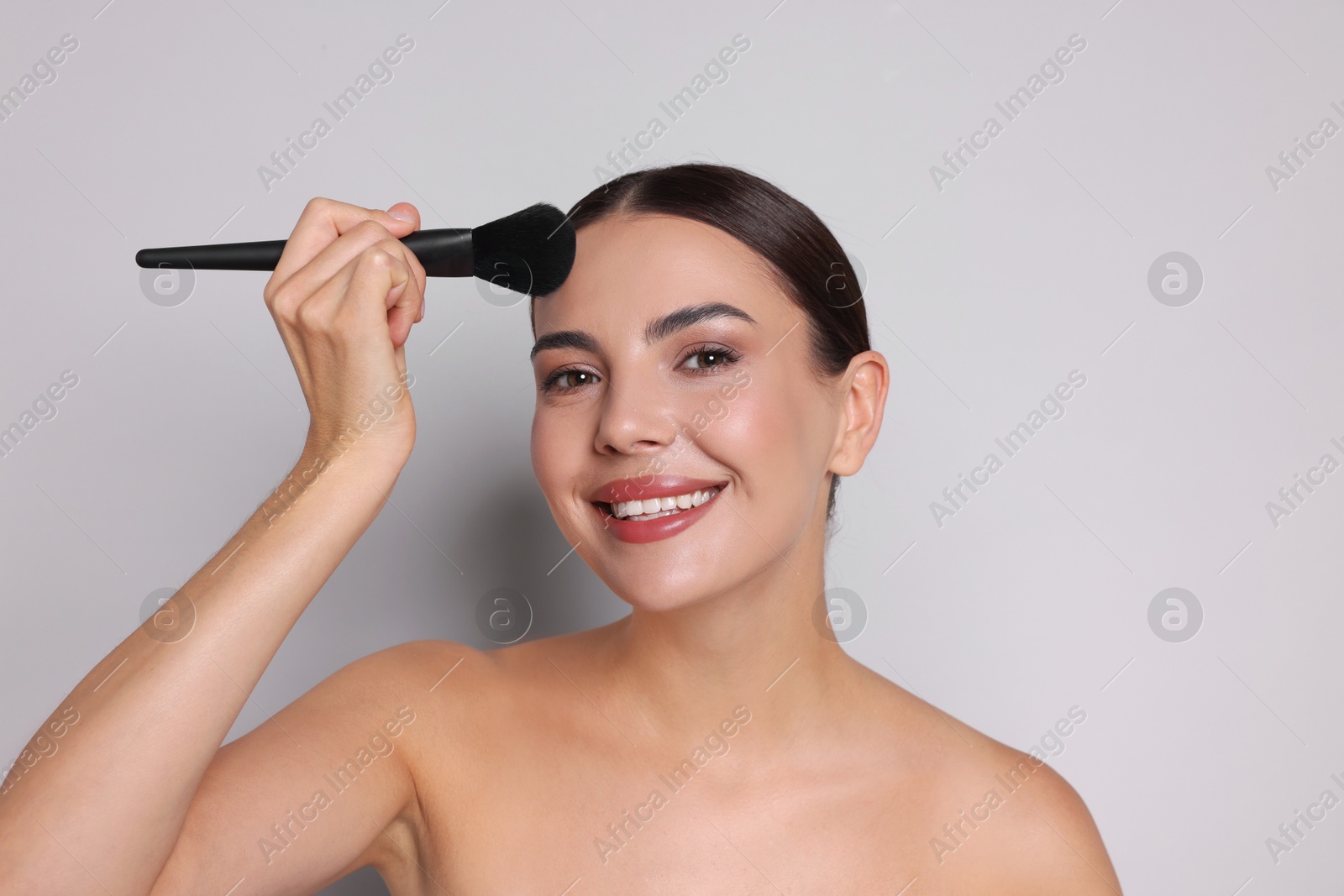 Beautiful woman applying makeup with brush on light grey background Photo of Beautiful woman applying makeup with brush on light grey background