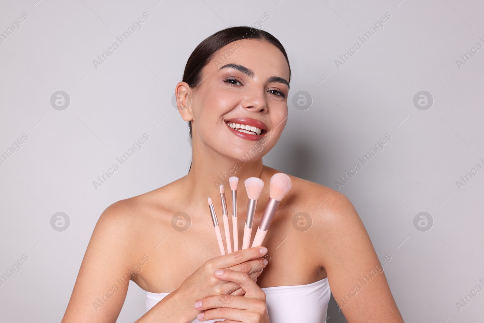 Beautiful woman with makeup brushes on light grey background Photo of Beautiful woman with makeup brushes on light grey background