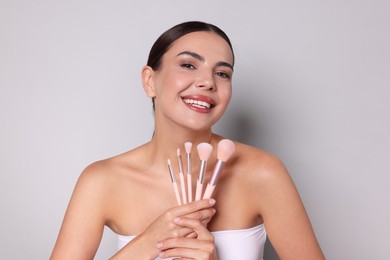Photo of Beautiful woman with makeup brushes on light grey background