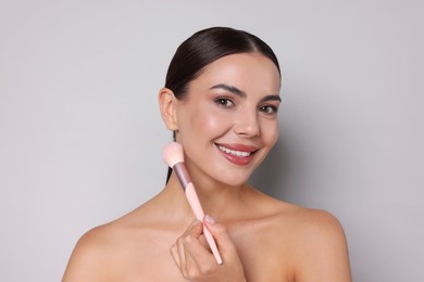 Photo of Beautiful woman with makeup brush on light grey background