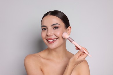 Photo of Beautiful woman applying makeup with brush on light grey background
