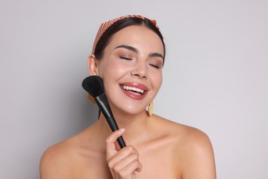 Photo of Beautiful woman with makeup brush on light grey background