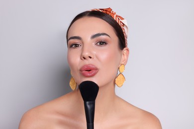 Photo of Beautiful woman with makeup brush on light grey background