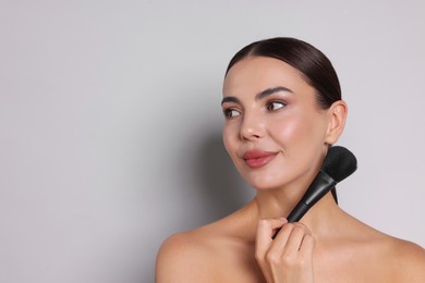 Photo of Beautiful woman with makeup brush on light grey background, space for text