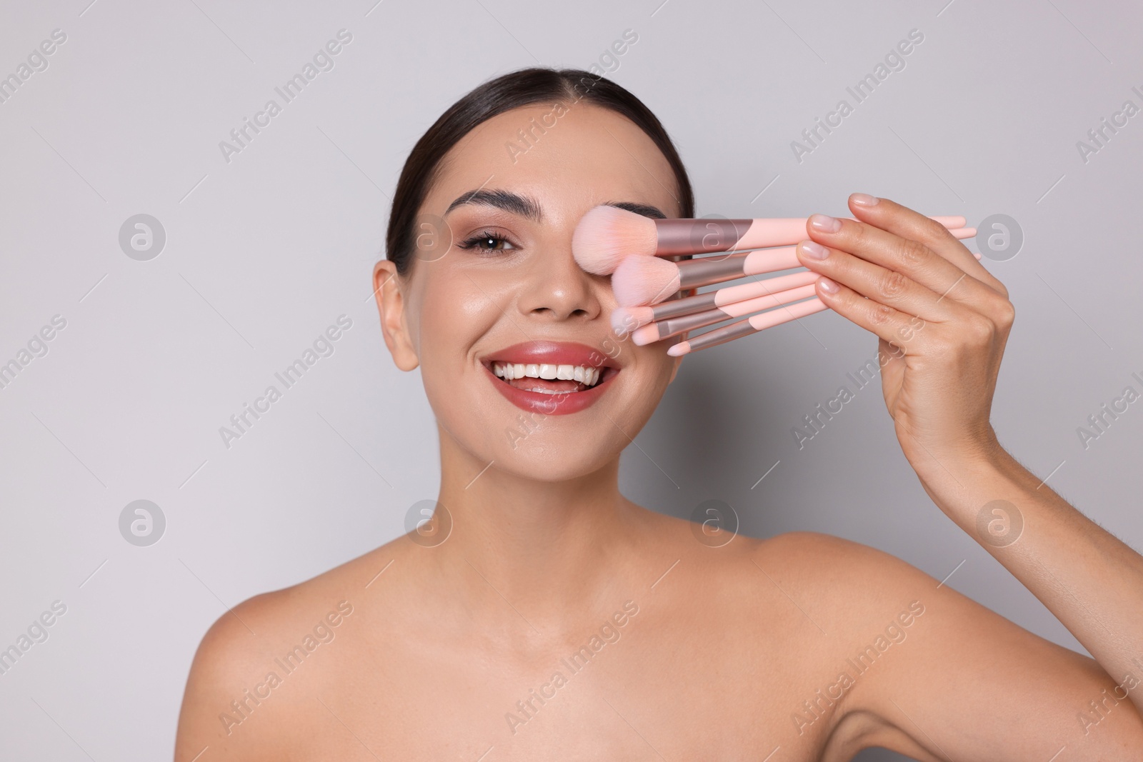 Beautiful woman with makeup brushes on light grey background Photo of Beautiful woman with makeup brushes on light grey background