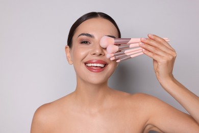 Photo of Beautiful woman with makeup brushes on light grey background