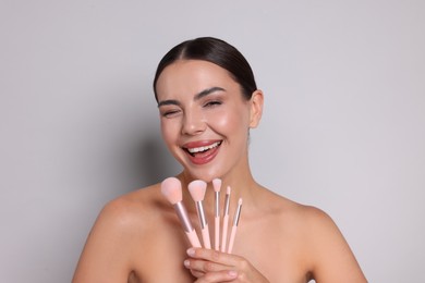 Photo of Beautiful woman with makeup brushes on light grey background