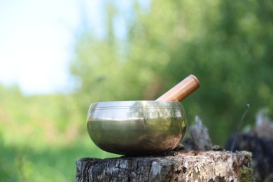 Photo of Tibetan singing bowl with mallet on tree stump outdoors