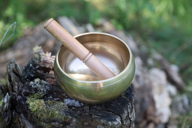 Photo of Tibetan singing bowl with mallet on tree stump outdoors, closeup