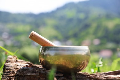 Photo of Tibetan singing bowl with mallet on piece of wood outdoors