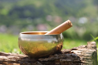 Photo of Tibetan singing bowl with mallet on piece of wood outdoors, closeup