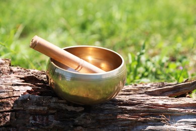 Photo of Tibetan singing bowl with mallet on piece of wood outdoors, closeup